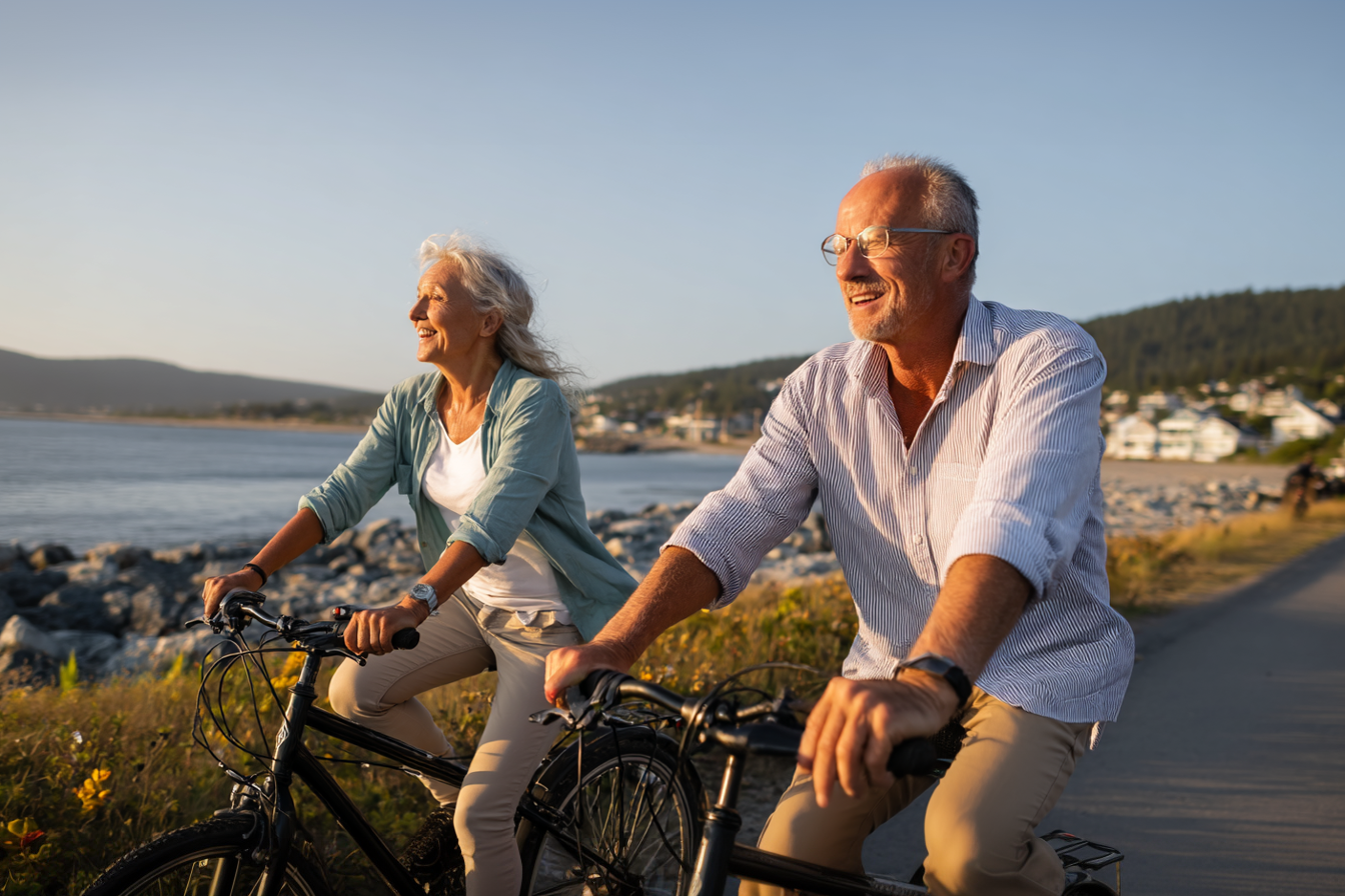 Happy retired couple cycling along a scenic coastal path, enjoying their worry-free retirement